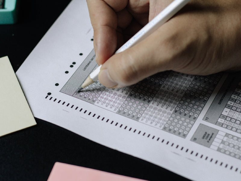 Main remplissant une grille de test avec un crayon, illustrant les quiz pour évaluer l’anxiété et l’éreutophobie